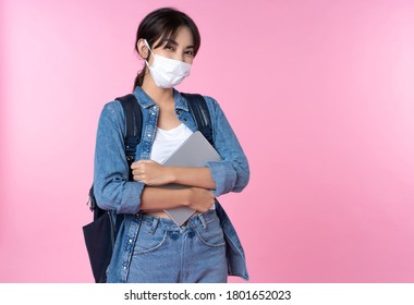 Portrait of young Asian college student wears face mask with laptop and backpack isolated over pink background - Powered by Shutterstock