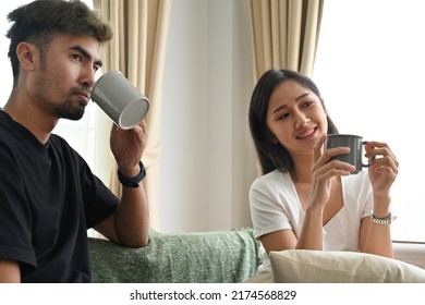 Portrait with Young Asian couple drinking a hot drink with mug while looking on a TV, Domestic life and Domestic home concept.
