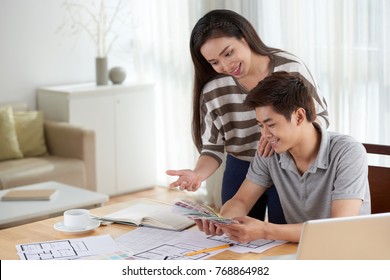 Portrait of young Asian couple gathered together at cozy living room and choosing colors while planning new house design - Powered by Shutterstock