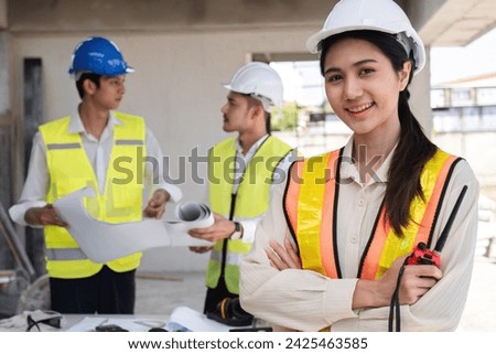 Portrait of a young Asian engineer standing with her arms crossed at a construction site. Portrait of successful young female engineer standing, smiling and looking at camera in engineer's uniform