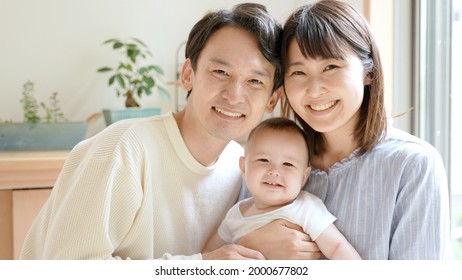 Portrait Of Young Asian Family With Baby Relaxing In The Living Room