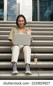 Portrait of young asian girl, student talks at laptop, video chat, speaking during online meeting, sitting outdoors on stairs. - Shutterstock ID 2233829827