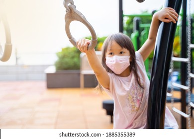 Portrait Of Young Asian Girl Wearing Mask Playing Outdoor Swinging On Monkey Bar Rings Having Fun