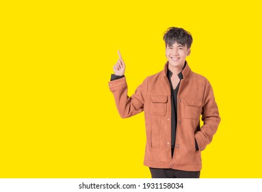 Portrait of young asian handsome man in fashionable clothing and standing posing pointing up with the index finger a great idea isolated on yellow background. Happy youth boy smiling in studio.
