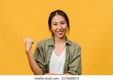 Portrait of young Asian lady smiling with cheerful expression, shows something amazing at blank space in casual cloth and looking at camera isolated over yellow background. Facial expression concept. - Shutterstock ID 2173600073