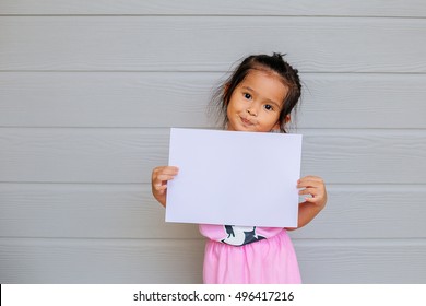 Portrait Of A Young Asian Little Girl Holding A Blank Sign White Paper On Wood Gray Background