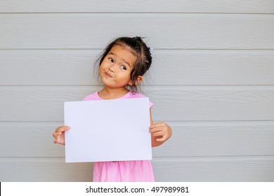 Portrait Of A Young Asian Little Girl Holding A Blank Sign White Paper On Wood Gray Background