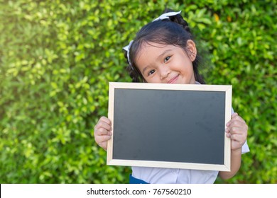 Portrait Of A Young Asian Little Girl Angry Holding A Blank Sign Blackboard In Public Park.