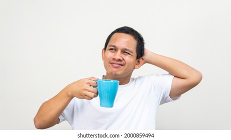 A portrait of young Asian Malay man stress thinking about a problem, scratching head while holding a cup of tea on isolated white backgrounds.