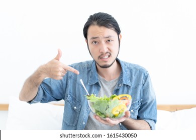 Portrait Of Young Asian Man Does Not Want To Eat And Has No Appetite Not Eat Salad. Adult Man Do Not Like To Eat Vegetables, Healthy Food, Vegetarian Products. Negative Displeased Face Expression.