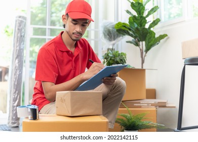 Portrait young Asian man house moving service worker in uniform doing home relocation, checking list cardboard boxes for preparing to move. Package delivery resident relocation moving service concept. - Powered by Shutterstock