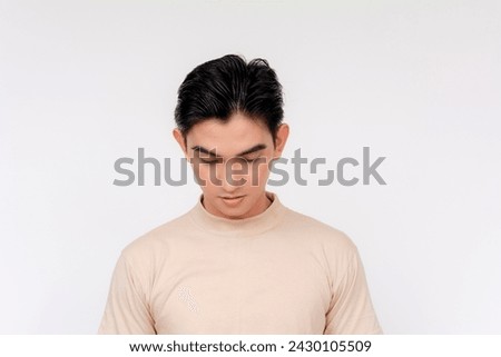 Portrait of a young Asian man looking downwards with a disappointed and regretful expression, isolated on a white background.