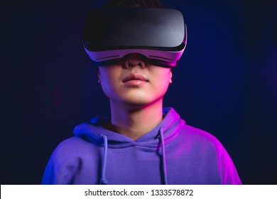Portrait of young Asian man playing VR game in dark blue background. Chinese young hipster wearing VR headset, half body shot. Young generation choose virtual reality relaxation concept.
