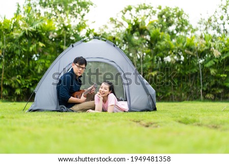 Portrait of a young Asian man playing guitar for his girlfriend. Happy young couple sitting near campfire and playing guitar