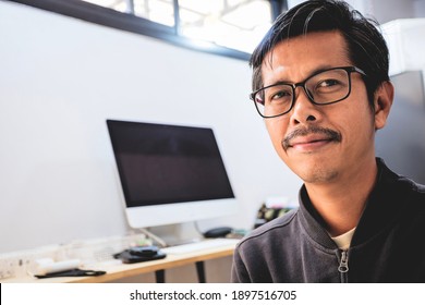 A Portrait Of A Young Asian Man Sitting At His Desk With A Computer.