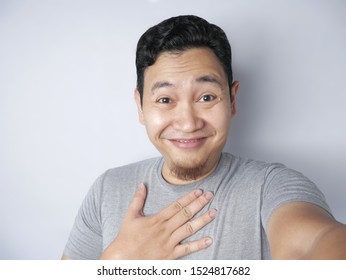 Portrait Of Young Asian Man Smiling While Taking Selfie Photograph Of Himself On His Smart Phone With Funny Expression