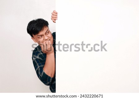 Portrait of young asian man standing behind an empty signboard with afraid face expression