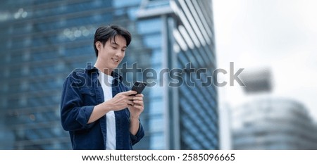 Portrait of young Asian man standing outdoor happy smiling use mobilephone.Handsome young asian man dressed casually walking spending time outdoors at city urban,carrying backpack,using mobile phone