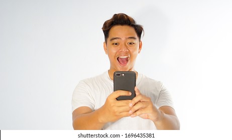 Portrait Of Young Asian Man Surprised By Media Content From Web Like Big Sale From Online Store On Display Of Her Smartphone, Isolated On White Background. Shock Content Concept