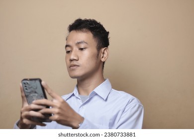 A Portrait of young Asian man using a smartphone isolated over cream background.