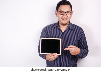 Portrait of young Asian man wearing eyeglasses and blue shirt smiling and presenting empty copy space blackboard