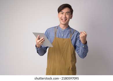 A Portrait Of Young Asian Man Wearing Apron Holding Tablet Over White Background Studio, Entrepreneur Concept