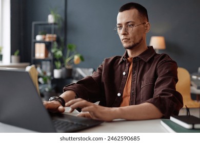 Portrait of young Asian man wearing glasses and using laptop in office with serious face expression - Powered by Shutterstock