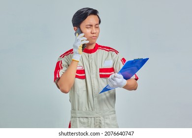 Portrait of young Asian mechanic talking on phone and holding clipboard with confused expression isolated on gray background - Powered by Shutterstock