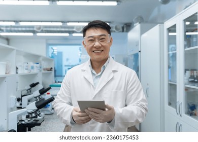 Portrait of a young Asian medical student. a scientist, a chemist who stands in the waiting room in a white coat and with a tablet in his hands, smiles at the camera. - Powered by Shutterstock