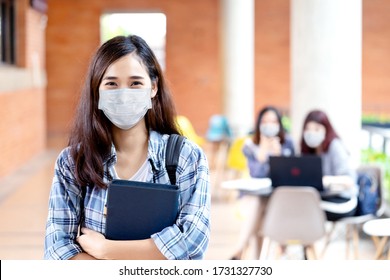 Portrait Of Young Asian Student Wear Mask Looking At Camera Holding Notebook Or Tablet In Arm In Concept Come Back Or Return To School, School Reopening And Unlock After Covid Or Coronavirus Outbreak.