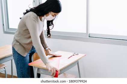 Portrait Of Young Asian Teacher Marking Places In The Classroom That Are To Be Empty After Students Return To School After Covid19 Quarantine And Lockdown. Social Distancing. Focus Hand.