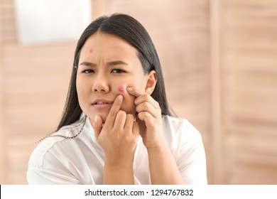 Portrait of young Asian woman with acne problem squishing pimples in bathroom