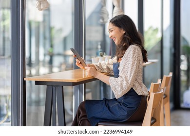 Portrait young Asian woman barista feeling happy smiling at urban cafe. Small business owner Asian girl in apron at small business entrance. - Powered by Shutterstock