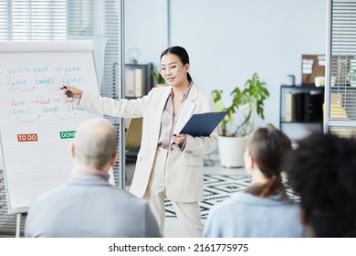 Portrait Of Young Asian Woman Giving English Lessons In Office Setting To Group Of People, Copy Space