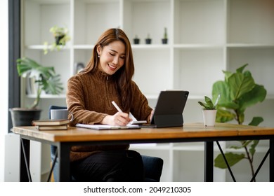 Portrait Of Young Asian Woman Hand Freelancer Is Working Her Job On Computer Tablet In Modern Office. Doing Accounting Analysis Report Real Estate Investment Data, Financial And Tax Systems Concept.