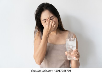 Portrait of young Asian woman has brain freeze after drink iced water.
female with a terrible headache with a glass of cold water on white background. Copy space