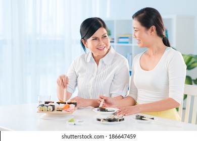 Portrait of young Asian woman and her mother eating sushi in the kitchen - Powered by Shutterstock