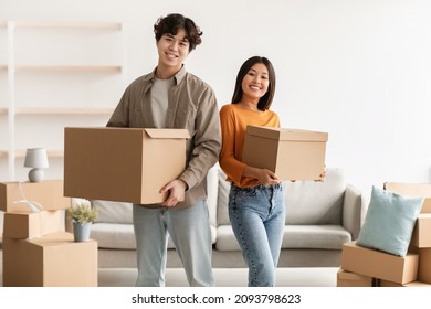 Portrait of young Asian woman and her cool boyfriend holding cardboard boxes, looking at camera and smiling in new home. Millennial spouses moving and settling into rented apartment - Shutterstock ID 2093798623
