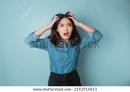 Portrait of young Asian woman isolated by blue background feeling frustrated with helpless face expression.