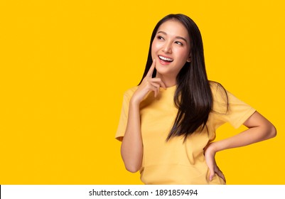 Portrait young asian woman look at copy space Beautiful girl wear yellow T shirt with yellow background at studio Pretty asia female get confident. Female get satisfied something Lovely lady get happy