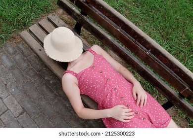 Portrait Of Young Asian Woman Lying On Bench With Hat On Her Face, Beautiful Chinese Girl In Sexy Red Dress Enjoy Her Carefree Time In Sunny Summer Day, High Angle View.