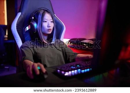 Portrait of young Asian woman playing video games in cybersports club with neon lights, copy space