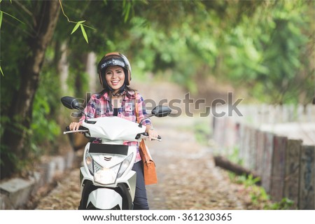 A portrait of a young asian woman riding a motorcycle in a park