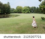 Portrait of young Asian woman running on grass field with barefoot in forest park, beautiful Chinese girl in white dress enjoy her carefree time in sunny summer day, full length shot.