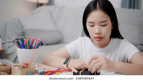 Portrait of Young Asian woman sitting on the floor wrapping a paper gift box in the living room ,Holiday hobbies, DIY crafts  - Powered by Shutterstock