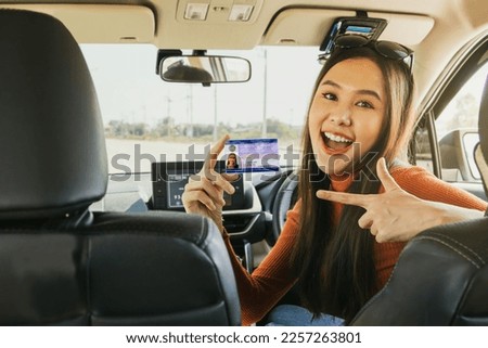 Portrait young asian woman sitting in her car show ownership of personal car license card passed test and pass exam pointing to new card with pride happy cheerful ready to drive carefree journey.