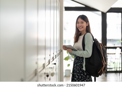 Portrait young asian woman student holding digital tablet at college standing in front of locker with backpack.