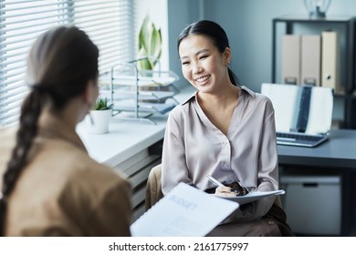 Portrait Of Young Asian Woman Talking To Colleague In Office And Smiling While Discussing Data Reports