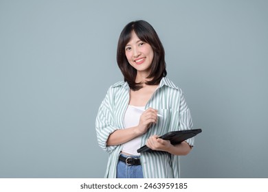 Portrait of young asian woman, teacher or student with digital tablet and pencil, writing, taking notes, doing her homework, standing over green background - Powered by Shutterstock