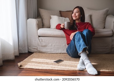 Portrait of a young asian woman using mobile phone and earphones to listening to music or online chatting at home - Powered by Shutterstock